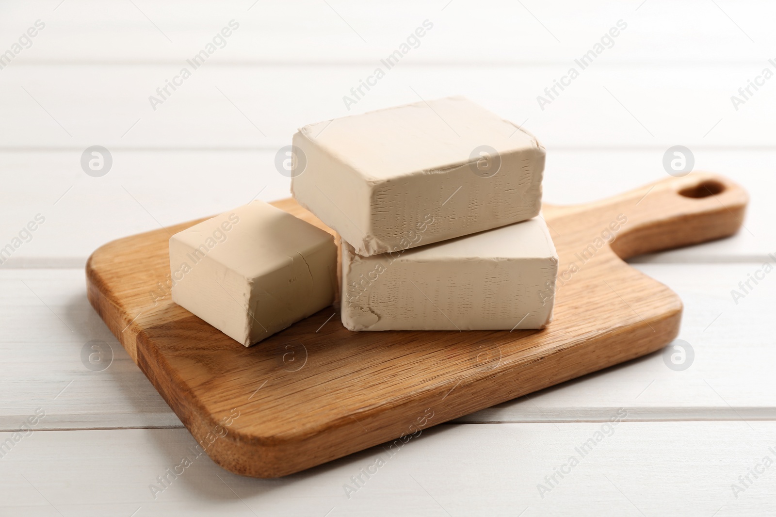 Photo of Blocks of compressed yeast with cutting board on white wooden table