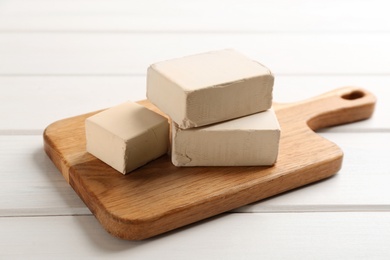 Photo of Blocks of compressed yeast with cutting board on white wooden table