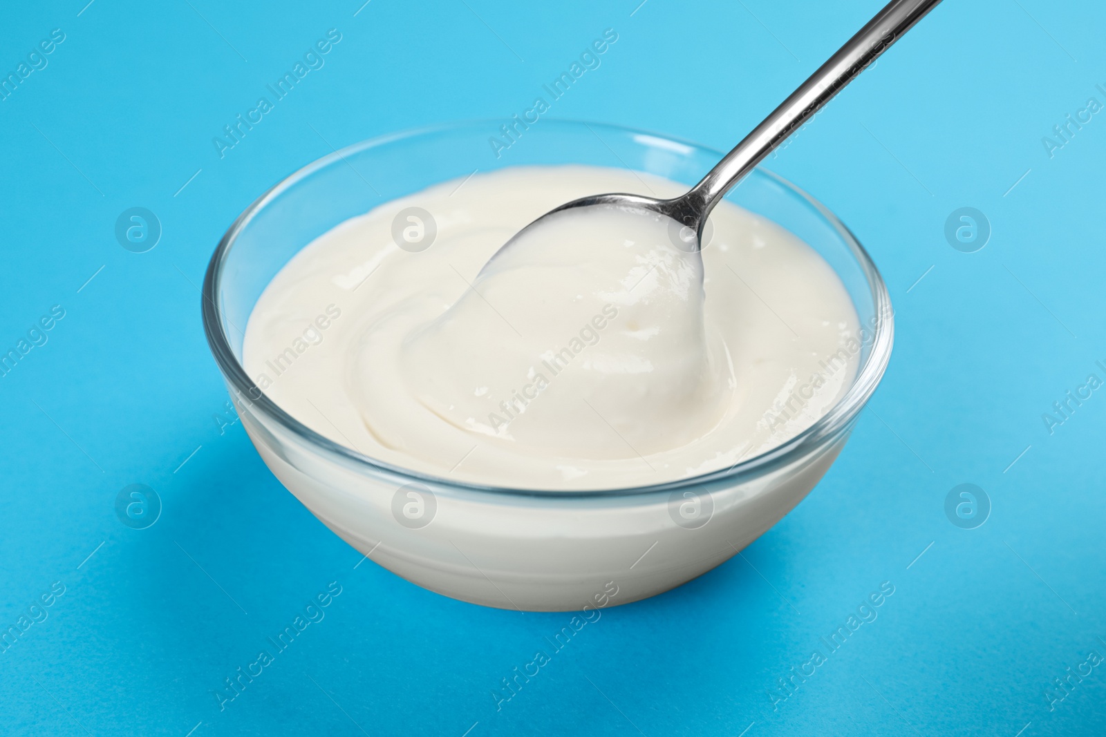 Photo of Eating tasty organic yogurt from bowl on light blue background