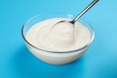 Photo of Eating tasty organic yogurt from bowl on light blue background