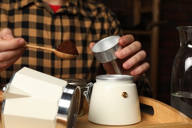Man putting ground coffee into moka pot at table indoors, closeup