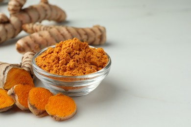 Aromatic turmeric powder and raw roots on white table, closeup. Space for text