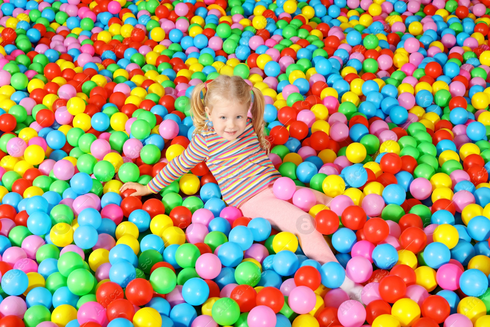 Photo of Cute child playing in ball pit indoors