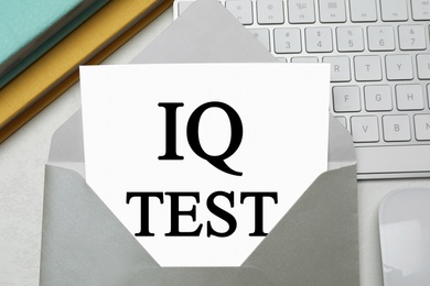 Paper with words IQ Test in envelope and keyboard on office table, flat lay