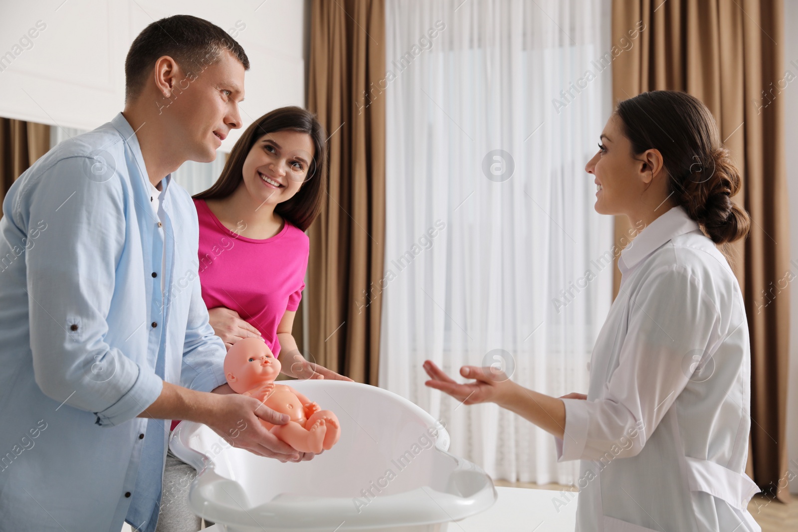 Photo of Man with pregnant wife learning how to bathe baby at courses for expectant parents indoors