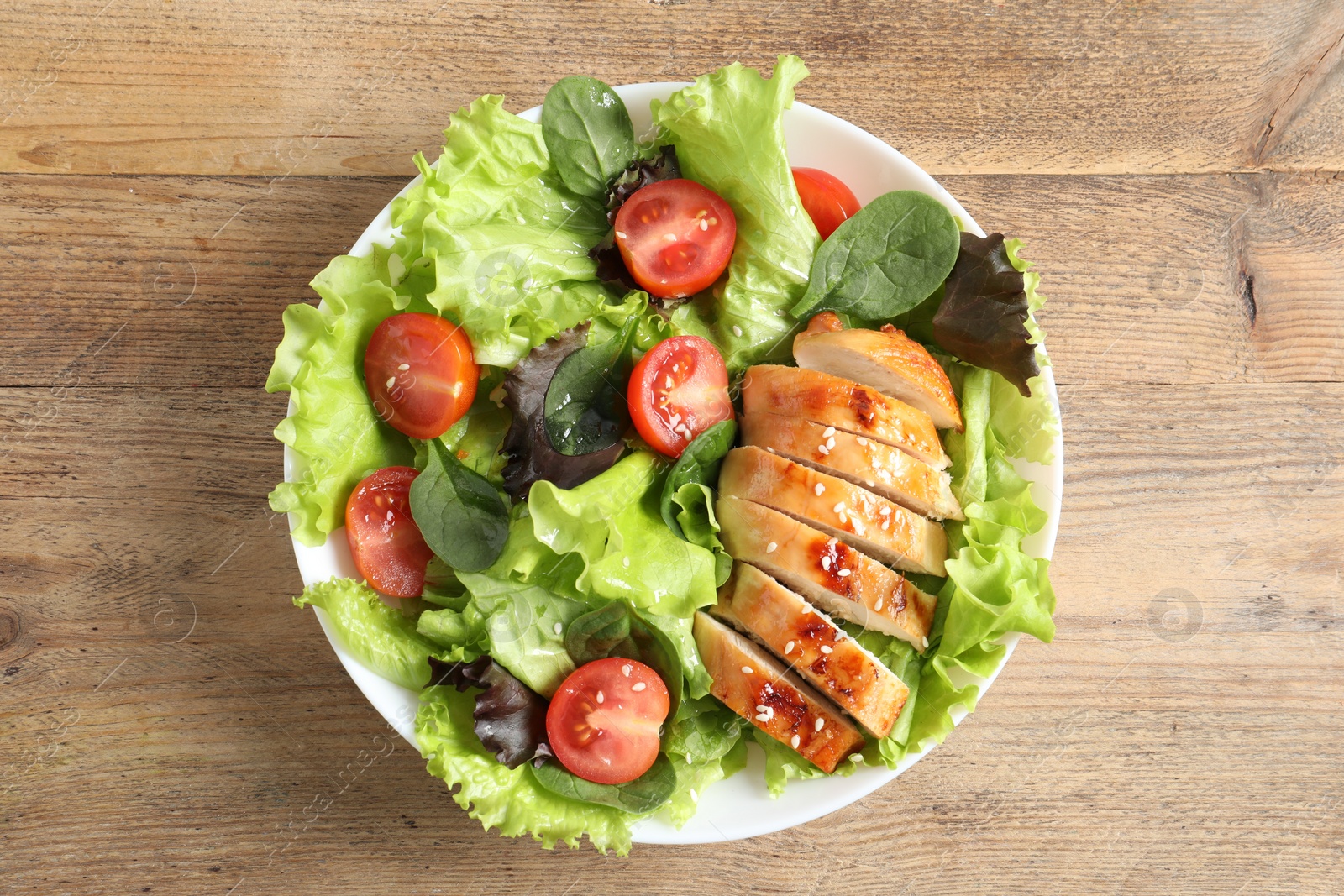 Photo of Delicious salad with chicken, cherry tomato and spinach on wooden table, top view