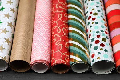 Photo of Different colorful wrapping paper rolls on grey wooden table, closeup