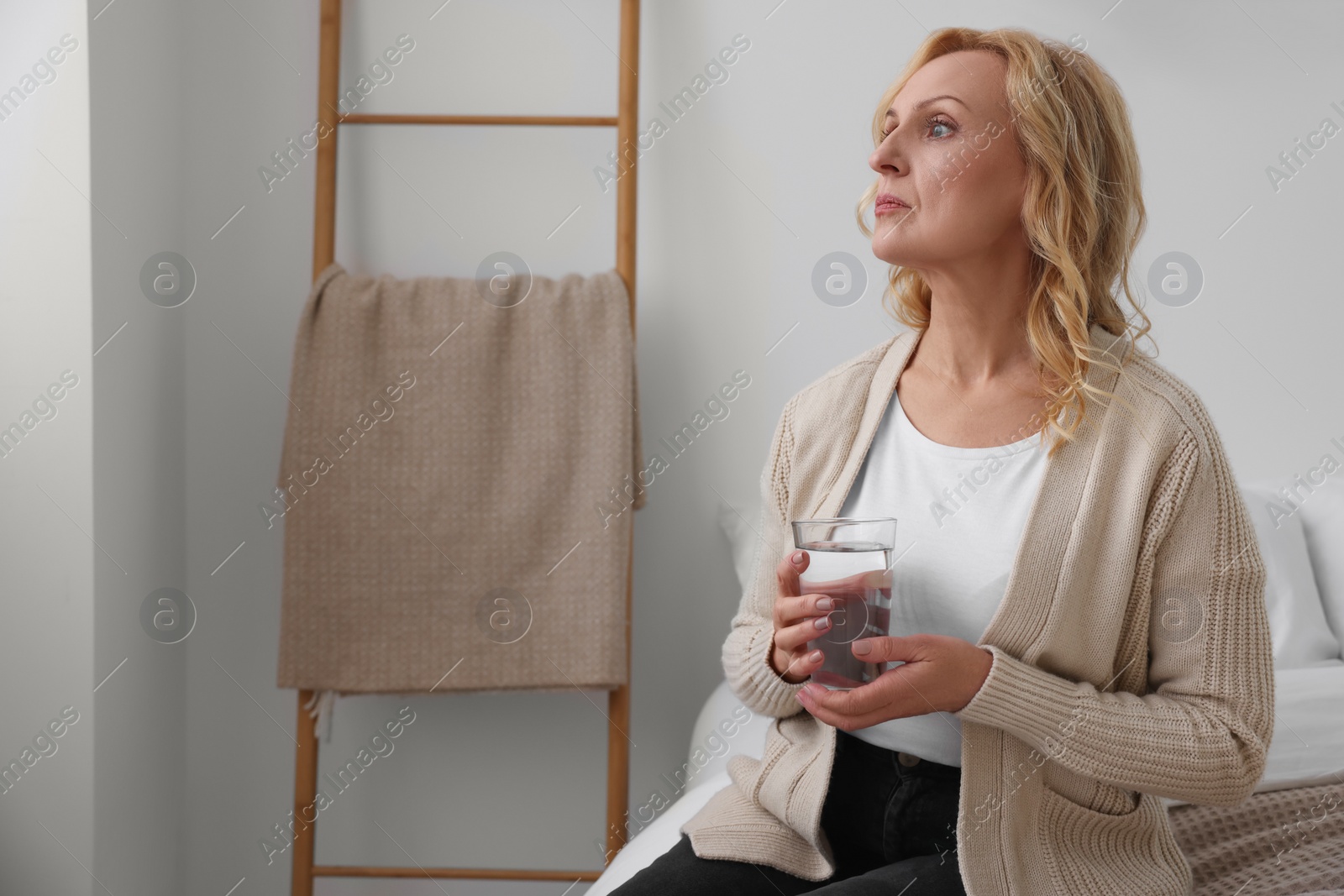 Photo of Upset middle aged woman with glass of water at home, space for text. Loneliness concept