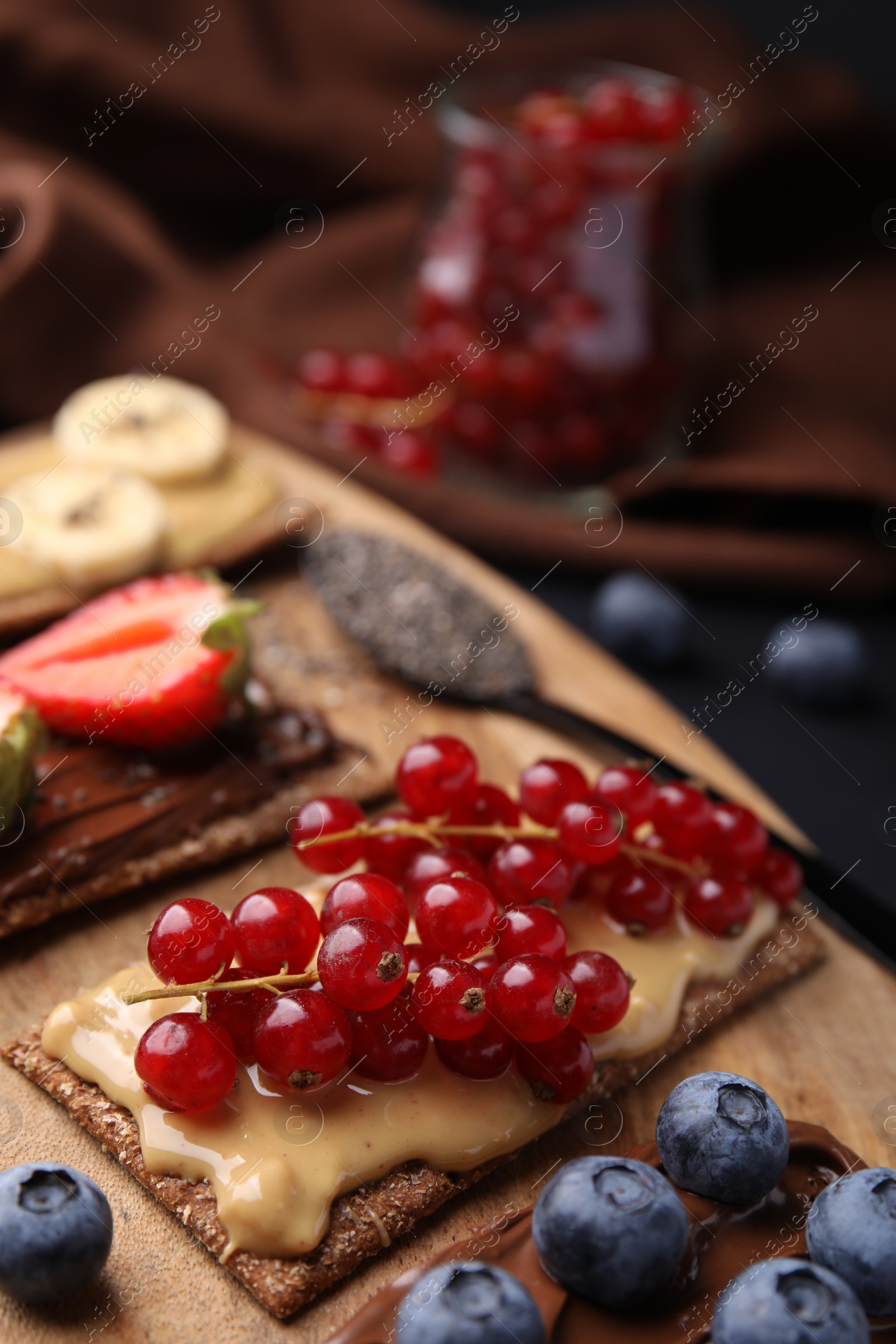 Photo of Fresh crunchy rye crispbreads with different toppings on wooden board, closeup