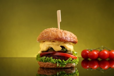 Delicious vegetarian burger and tomatoes on mirror surface against olive background