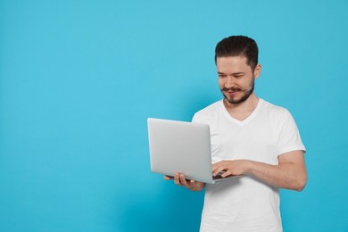 Photo of Smiling man using laptop on light blue background. Space for text