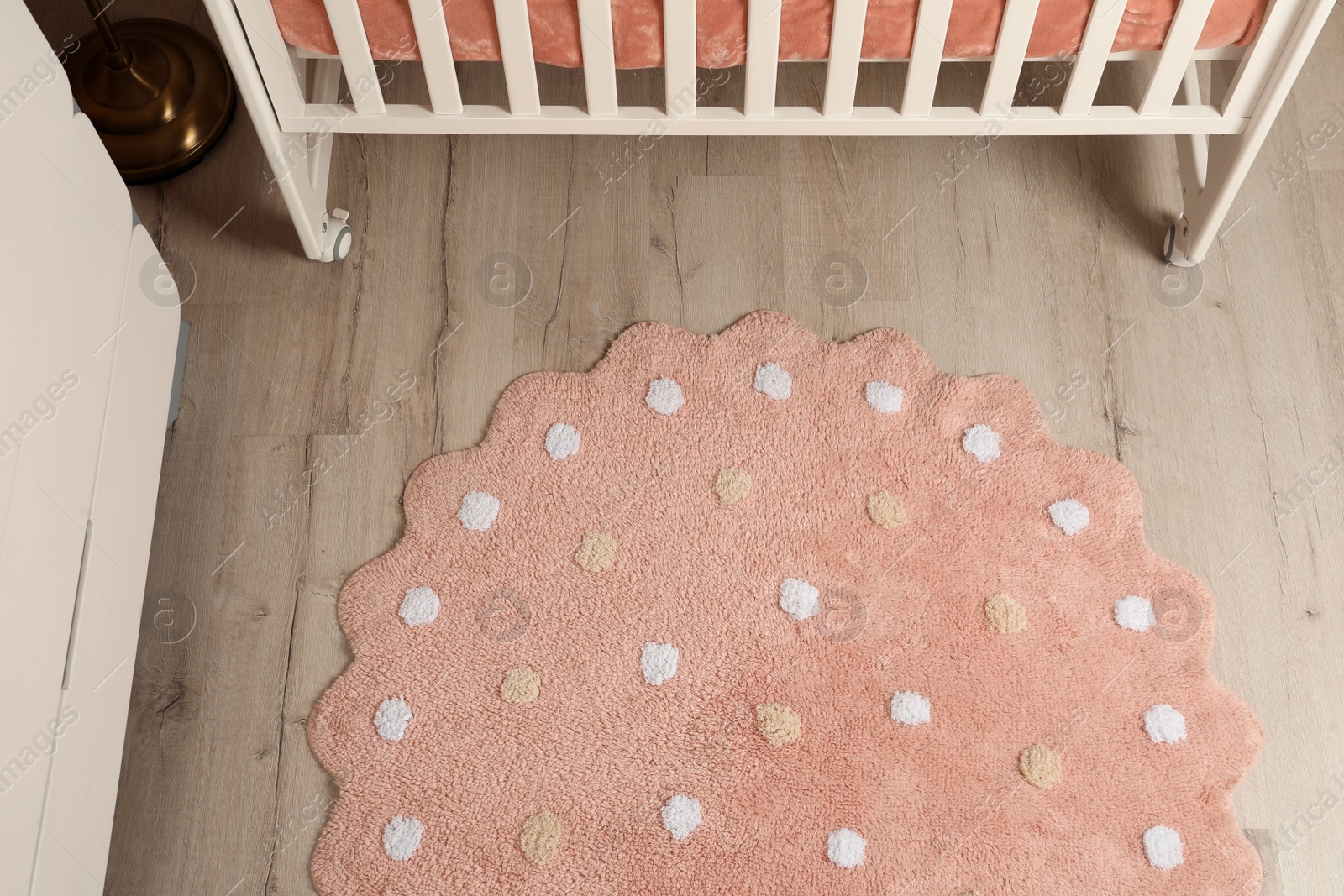 Photo of Round pink rug with polka dot pattern on wooden floor in baby's room, above view