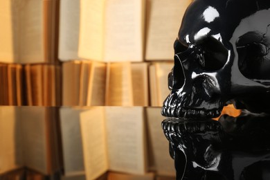 Black human skull on mirror table near books. Space for text
