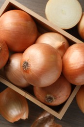 Whole and cut onions on wooden table, flat lay