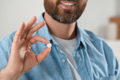 Man with pill on blurred background, closeup view