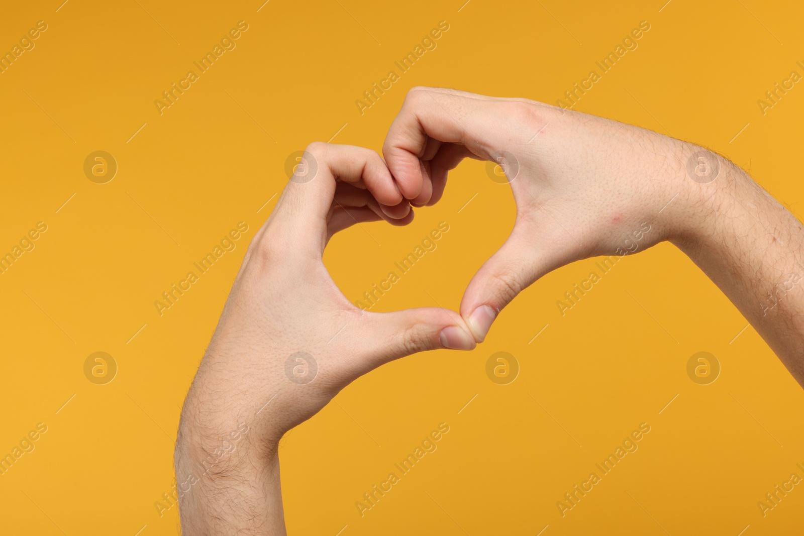 Photo of Man showing heart gesture with hands on golden background, closeup