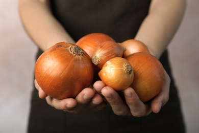 Photo of Woman holding ripe onions on grey background