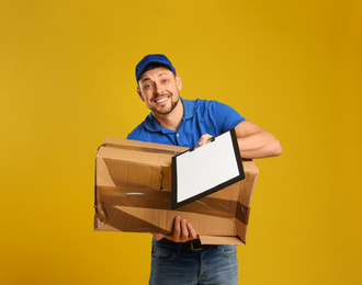 Photo of Emotional courier with damaged cardboard box and clipboard on yellow background. Poor quality delivery service