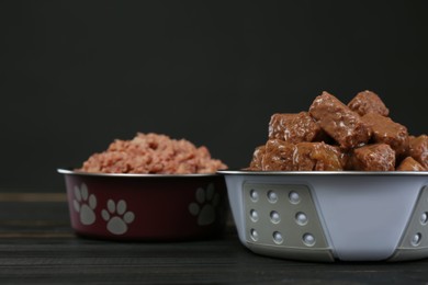 Photo of Different pet food in feeding bowls on wooden table against dark background, space for text