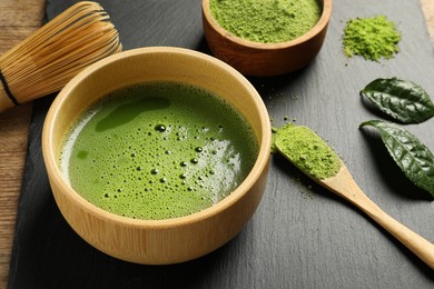 Photo of Cup of fresh matcha tea, green powder and bamboo whisk on table, closeup