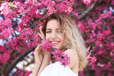 Attractive young woman posing near blossoming tree on sunny spring day