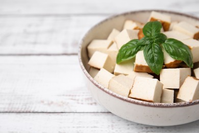 Photo of Bowl with delicious fried tofu and basil on white wooden table, closeup. Space for text