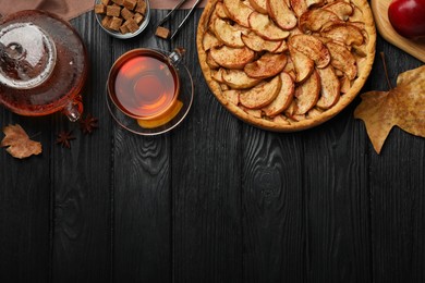 Photo of Delicious apple pie and aromatic tea on black wooden table, flat lay. Space for text