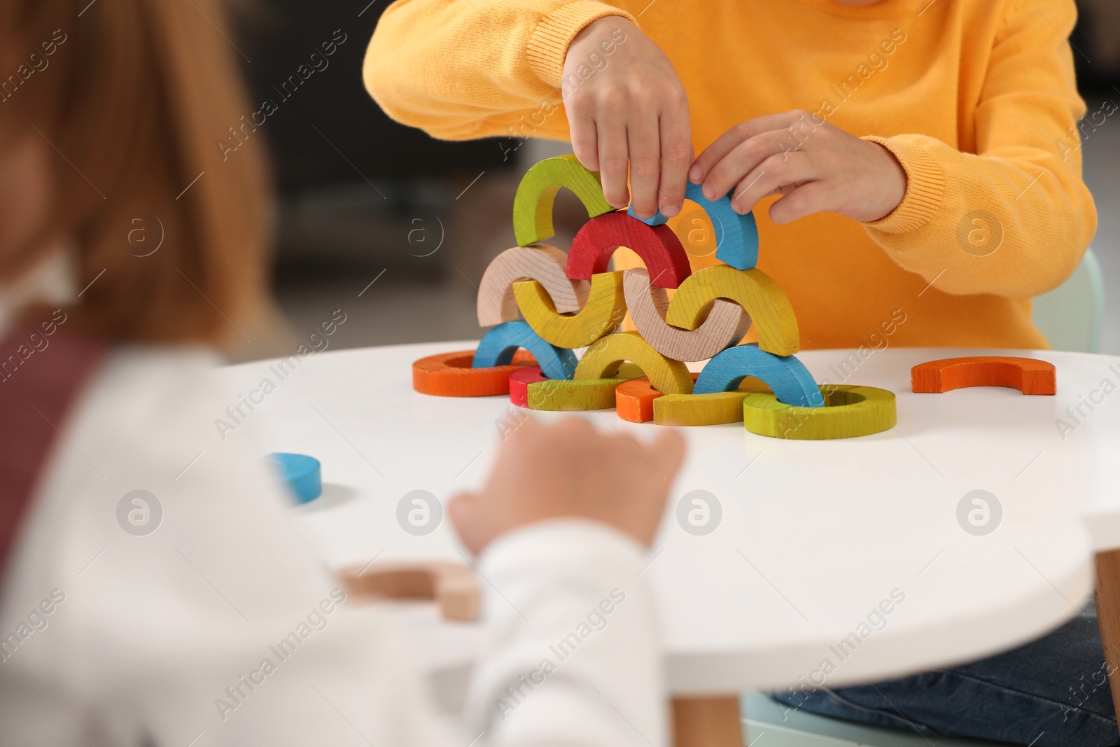 Photo of Little children playing with colorful wooden pieces at white table indoors, closeup. Developmental toy