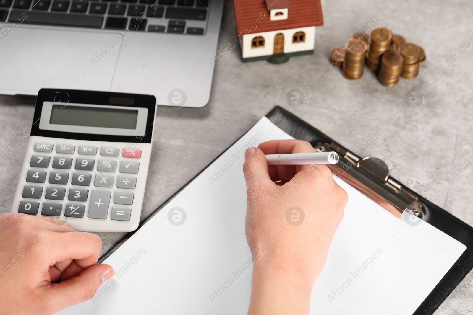 Photo of Woman planning budget, closeup. House model, calculator and coins on grey table