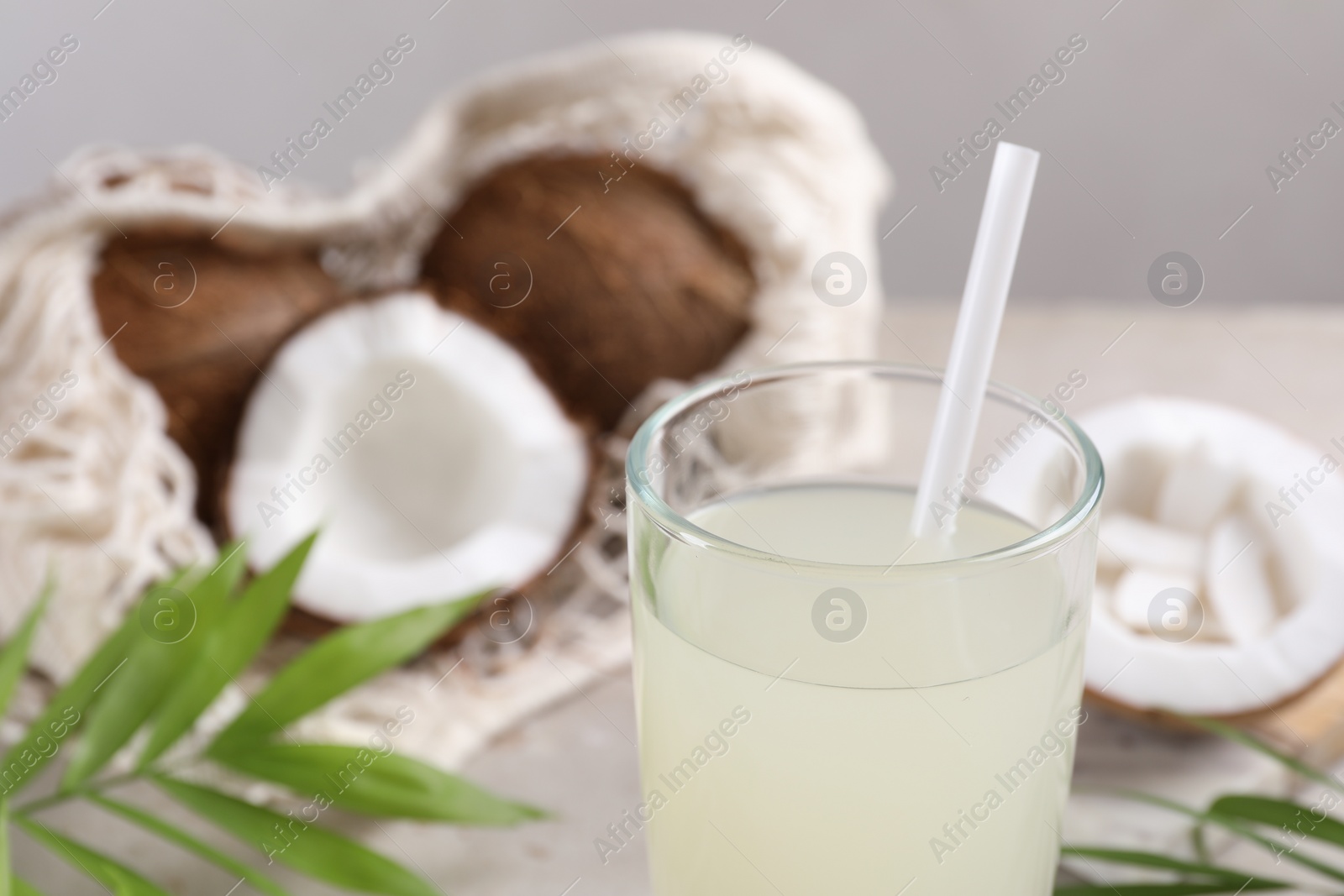 Photo of Glass of coconut water, palm leaves and nuts on light table, closeup