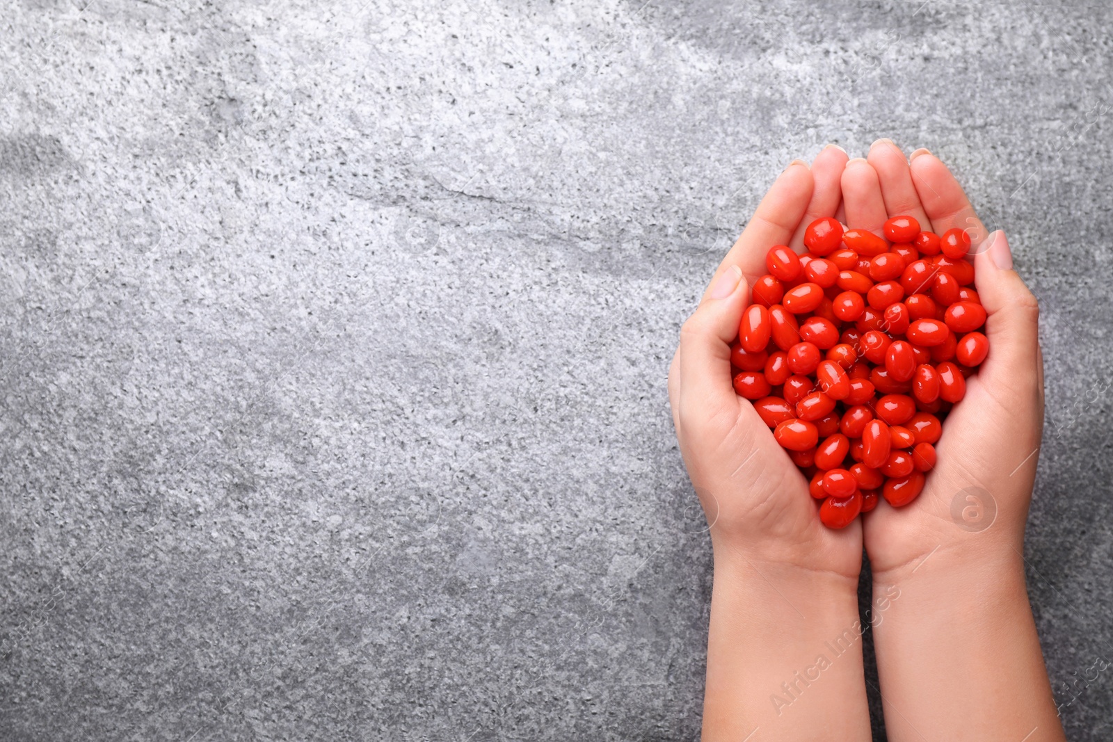 Photo of Woman holding fresh goji berries on grey background, top view. Space for text