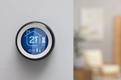 Image of Thermostat displaying temperature in Celsius scale and different icons. Smart home device on white wall, space for text