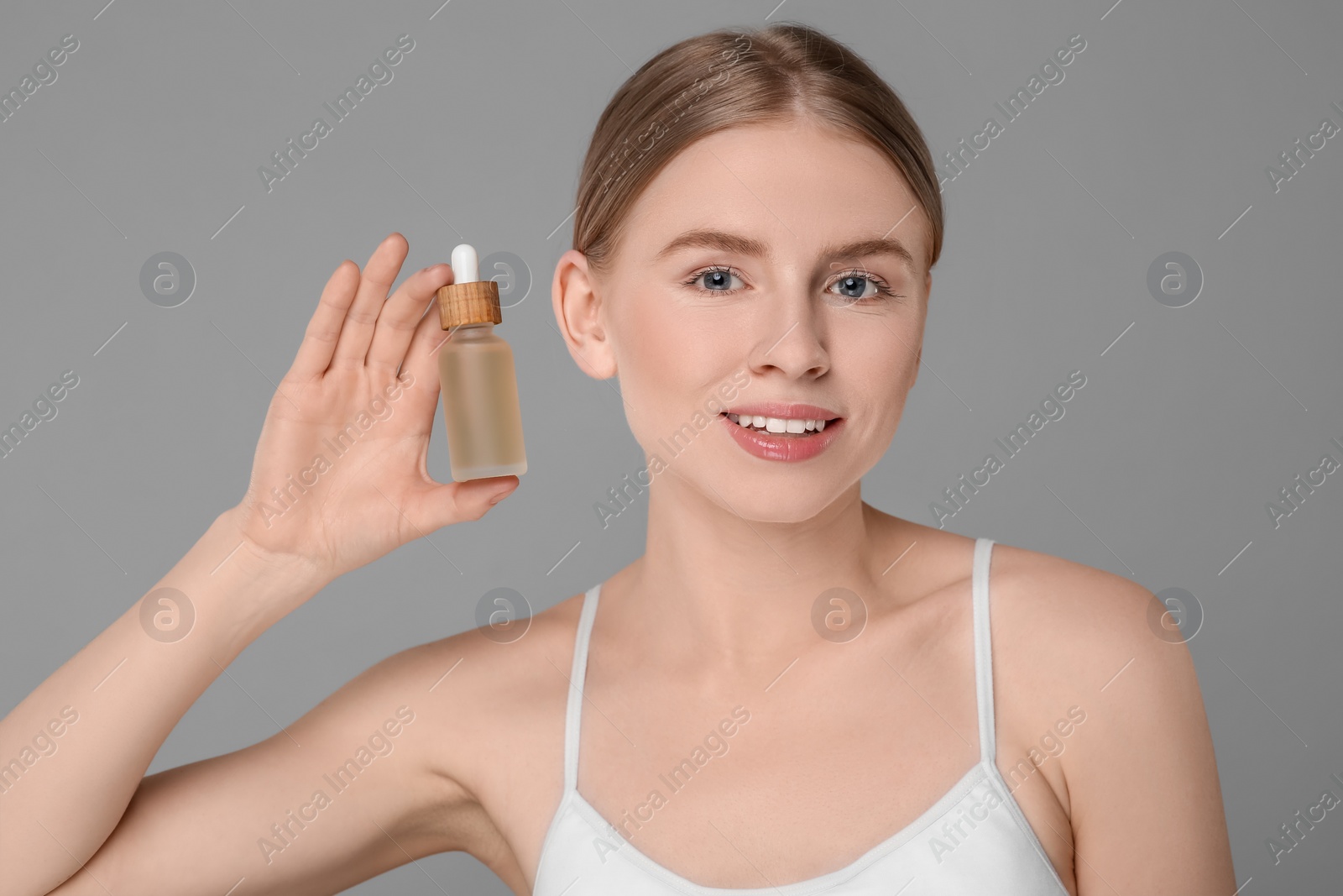 Photo of Beautiful young woman with bottle of essential oil on light grey background