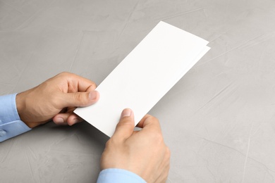 Photo of Young man holding blank brochure at grey table, closeup. Mock up for design