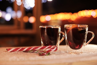 Glass cups of mulled wine and candy canes on table covered with snow outdoors. Space for text