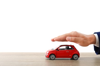Insurance agent holding hand over toy car on table against white background, closeup