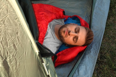 Photo of Young man resting in sleeping bag inside camping tent, above view