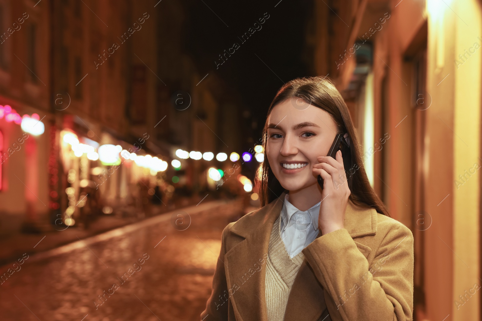 Photo of Smiling woman talking by smartphone on night city street. Space for text