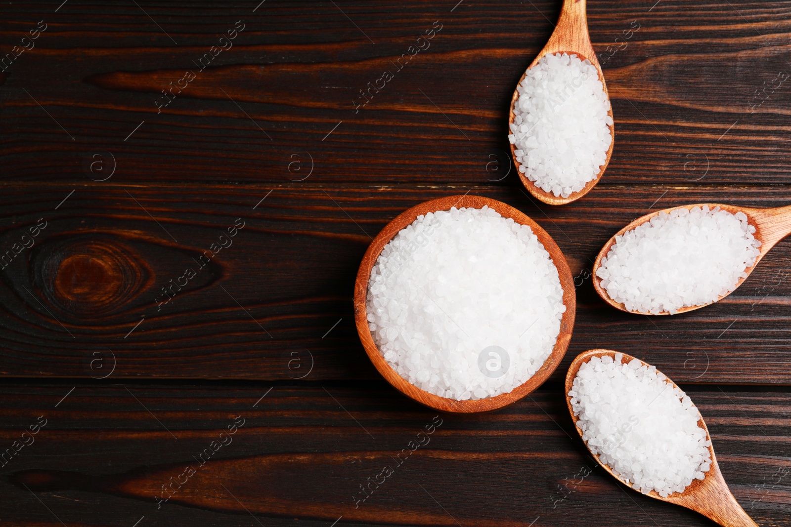 Photo of Bowl and spoons with natural sea salt on wooden table, flat lay. Space for text