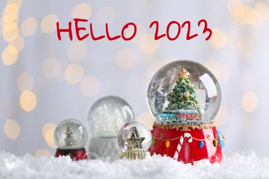 Image of Hello 2023. Beautiful snow globes against blurred Christmas lights