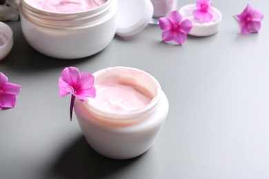 Jars of body cream and flowers on grey background