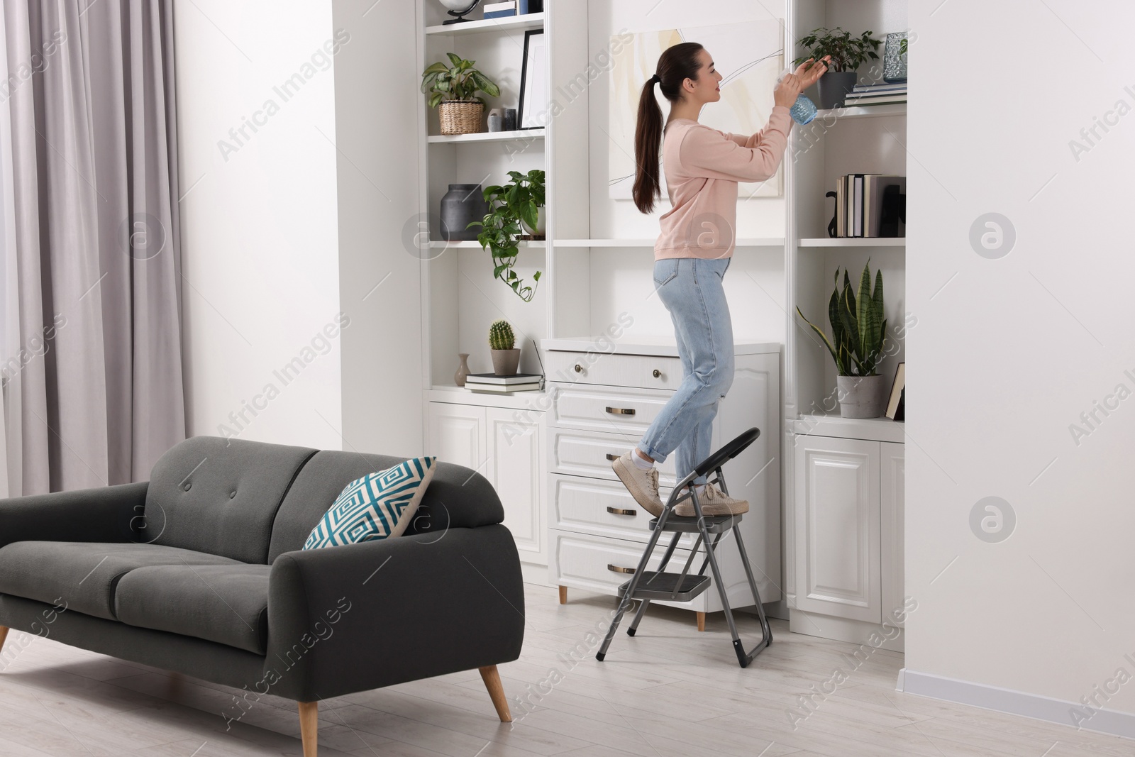 Photo of Woman on ladder watering houseplant at home