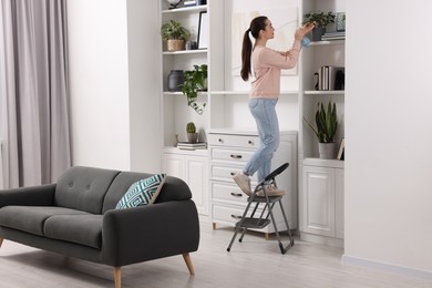 Woman on ladder watering houseplant at home