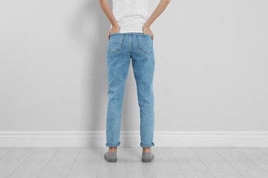 Photo of Young woman in stylish jeans near light wall, closeup