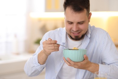 Photo of Smiling man eating tasty cornflakes at breakfast indoors