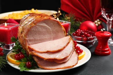 Photo of Delicious Christmas ham served with garnish on dark table