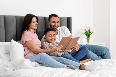 Happy international family reading book on bed at home