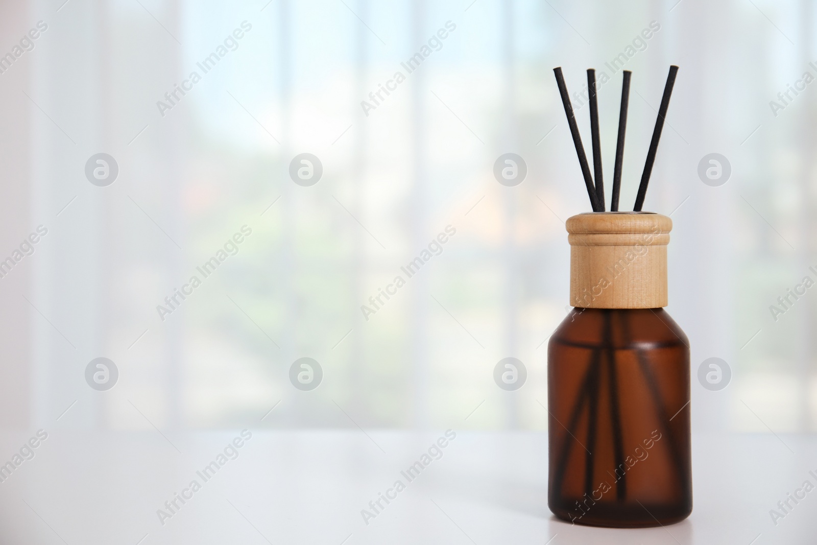 Photo of Reed diffuser on white table against window in room. Space for text