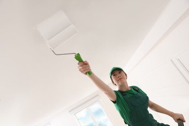 Photo of Worker painting ceiling with white dye indoors