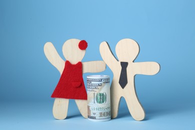 Photo of Gender pay gap. Wooden figures of man and woman with dollar banknote on light blue background